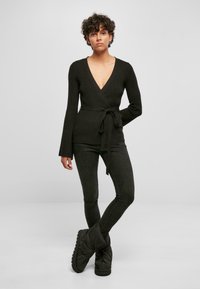 Svart wrap-around topp med lange ermer, v-utringning og knytt belte i midjen, kombinert med mørke skinny jeans og store svarte støvler.