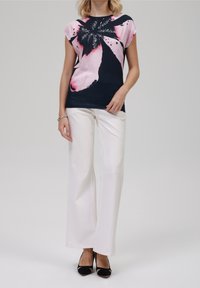 Marinblå t-shirt med rosa blommönster, korta ärmar, i kombination med vita vida byxor och svarta klackar. Slät tygtextur.