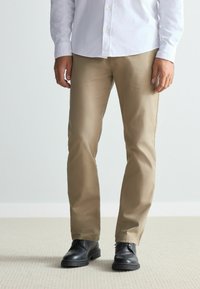 Beige, straight-leg pants made from cotton blend fabric, paired with black leather shoes, displayed in a standing position.