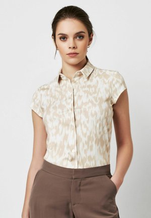 Kurzärmliges Hemd mit Knöpfen in hellem Beige mit abstrakten weißen Mustern, aus glattem Stoff. Kombiniert mit braunen Hosen in entspannter Passform.