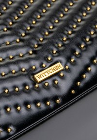 Schwarze Lederhandtasche mit erhabenen goldfarbenen Nieten und einer strukturierten Musterung. Vorderseite mit einer goldenen WITTCHEN-Logoplatte versehen.