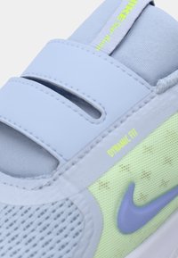 Chaussure de sport bleu clair avec une tige en maille, des sangles Velcro et des accents vert fluo. Présente un swoosh Nike violet et la marque "DYNAMIC FIT".
