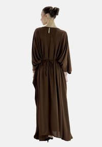 Robe maxi marron avec une coupe ample, des manches bracelet, un détail de taille à nouer, et une fermeture par trou de serrure à l'arrière. Tissu doux avec une texture fluide.