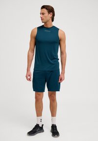 Camisa atlética sin mangas en color teal para hombre, combinada con shorts a juego, que presenta una tela suave, un diseño minimalista y sin logotipos visibles.