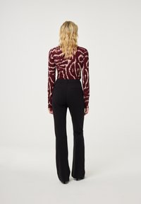 Bordeauxgekleurde top met lange mouwen en een zwart gepaste flarebroek. De top heeft abstracte ontwerpen; de broek heeft een gladde textuur met zakken.