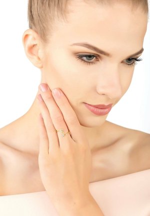 Gold ring with a minimalist design featuring an accent stone. Model's hand is gently touching her face, highlighting the ring's detail.