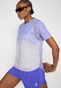 Μωβ αθλητικό τοπ με βαθμιαία μετάβαση σε ανοιχτό γκρι, με διακοσμητικό μοτίβο. Συνδυάζεται με μπλε σορτς, και τα δύο από ελαφρύ ύφασμα.