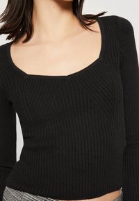 Svart ribbat långärmat tröja med bred fyrkantig halsringning och texturerade mönsterdetaljer, figurnära design.