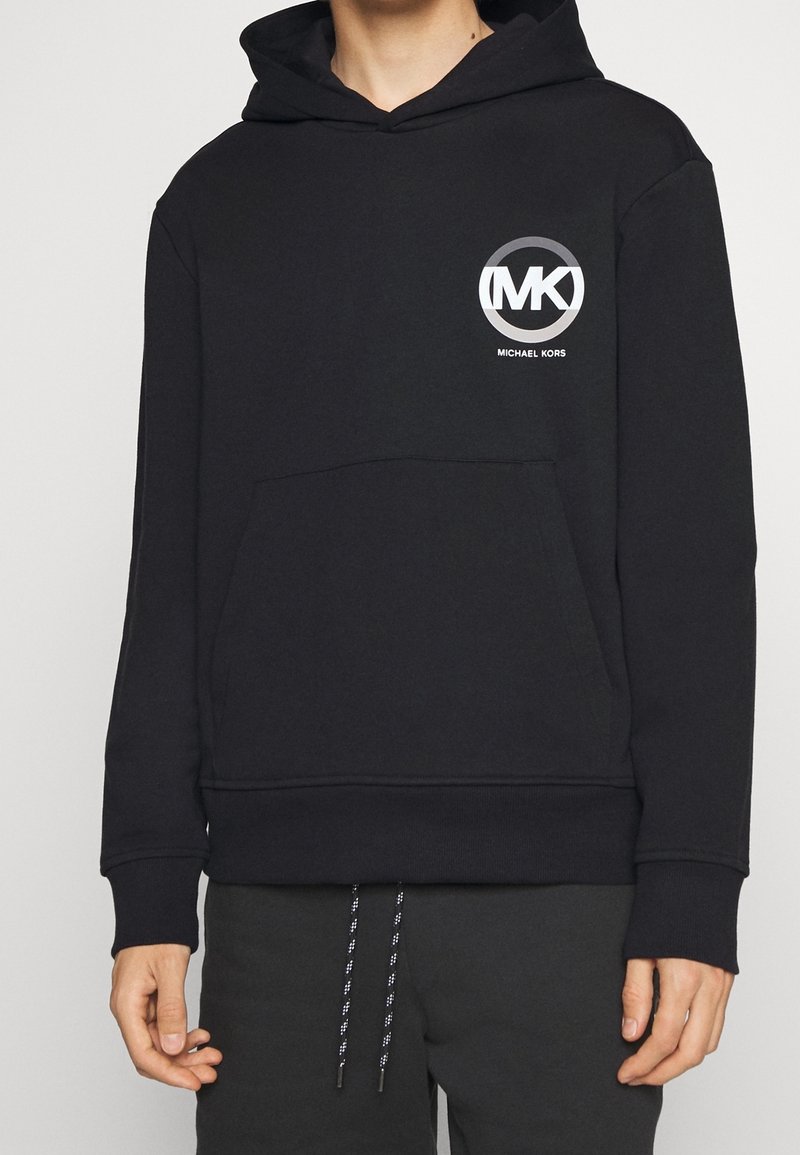 Black hoodie made of cotton blend, featuring a front pocket and a circular logo with "MK" and "MICHAEL KORS" in white. Simple design.