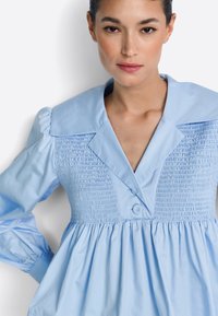 Vestido de algodón azul claro con corpiño fruncido, cuello grande y cierre de botones, con mangas abullonadas y falda fruncida.