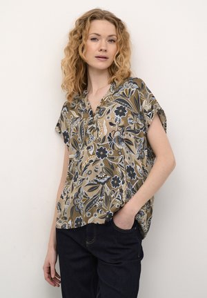 Blumenmuster-Bluse mit kurzen Ärmeln in Erdtönen und V-Ausschnitt, verziert mit filigranen blau-weißen Mustern, kombiniert mit dunkelblauen Jeans.