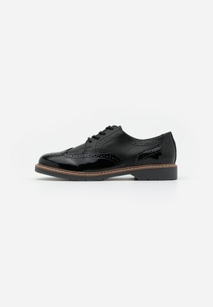 Chaussure oxford en cuir noir avec une finition brillante, des détails brogues, une semelle plate et des coutures brunes le long du bord. Design classique à lacets.