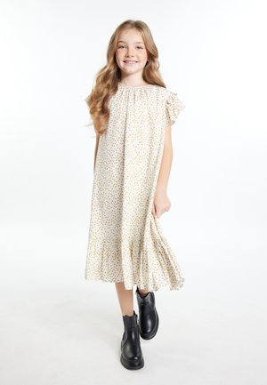 Weißes Kleid mit gelbem Blumenmuster, kurzen Rüschensäumen und einem ausgestellten Saum. Getragen mit schwarzen Knöchelstiefeln. Glatte Stoffstruktur.