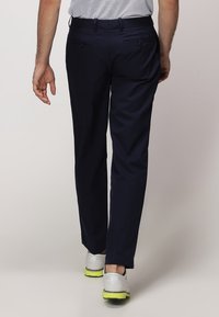 Námořnické modré kalhoty s elegantním střihem, které mají zadní kapsy a hladkou texturu, spárované s bílými botami s akcentem zelených podrážek.