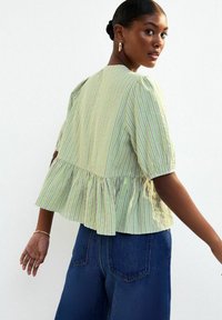 Groen gestreepte blouse met een peplumzoom, voorzien van korte puffmouwen en een geweven katoenen stof. Gekocht in combinatie met hoog getailleerde donkerblauwe jeans.