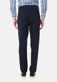 Pantaloni di cotone blu navy con vestibilità dritta, dotati di tasche posteriori e passanti per cintura. Abbinati a una camicia a righe bianche e nere.