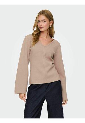 Pull léger beige en V avec des manches longues légèrement évasées et une texture lisse, associé à un pantalon en denim foncé.