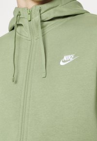 Sweat à capuche Nike vert clair avec fermeture éclair sur le devant et cordons, avec un petit logo blanc Nike sur la poitrine.