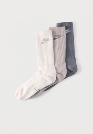 Trois chaussettes Nike montantes en blanc, gris clair et gris foncé, chacune avec le logo Nike près du haut du bord.