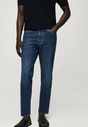 Jeans de mezclilla azul oscuro con corte recto, diseño de cinco bolsillos y costuras visibles. Combinados con sandalias negras tipo slip-on.