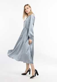 Sukienka midi z satyny w delikatnym niebieskim kolorze, z długimi rękawami, talią podkreśloną wcięciem i zwiewnym dołem, w zestawieniu z czarnymi szpilkami z złotymi akcentami.