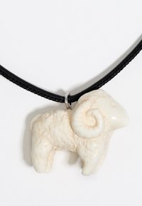Ceramiczny wisiorek w kształcie ram w kremowobiałym kolorze z teksturową powierzchnią, przymocowany do plecionego czarnego sznurka za pomocą małego metalowego pierścienia.