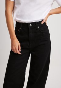 Svarta högmidjade jeans i denim med knappstängning framtill, två framfickor och en texturerad tyg.