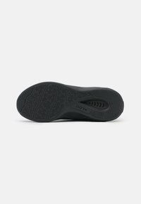 Semelle de chaussure de sport noire avec un caoutchouc texturé pour une meilleure traction, présentant un motif géométrique et une ventilation circulaire pour la respirabilité.