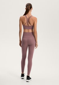 Mavri športni modrček s križnimi naramnicami in usklajenimi visokimi leginami, oba izdelana iz gladkega, raztegljivega materiala, v kombinaciji s črnimi športnimi čevlji.