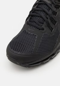 Shoe atlético preto com um cabedal em malha e texturas destacadas, biqueira reforçada e uma sola acolchoada para conforto e suporte.