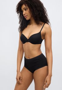 Μαύρο επενδεδυμένο σουτιέν με λεπτές ράντες και λεπτομέρεια φιόγκου στο κέντρο, συνδυασμένο με ψηλόμεσο μαύρο σλιπ με κυματιστά τελειώματα.