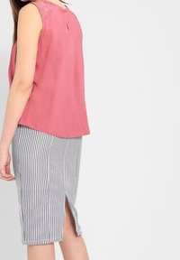 Top rosso senza maniche con dettagli in pizzo sul colletto, abbinato a una gonna a tubo a righe blu navy e bianche, lunga fino al ginocchio, con uno spacco frontale.