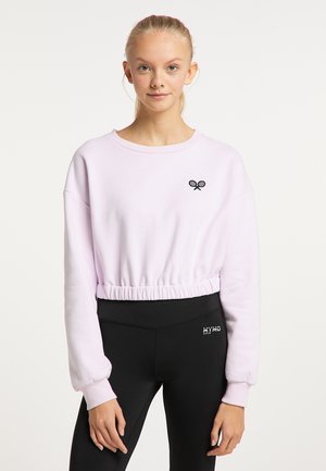 Világos rózsaszín, cropped pulóver, összegyűrt derékkal, kis fekete teniszütőt ábrázoló emblémával a mellrészen, fekete leggingsszel párosítva.