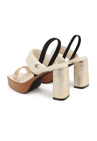 Sandalias de plataforma bicolor con un upper crema, acentos dorados en el tacón y tiras negras. Los tacones gruesos tienen forma cuadrada y un acabado brillante.