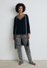 Čierny loungewear set s dlhým rukávom, V-výstrihom a vzorovanými nohavicami. Materiál vyzerá jemne s plynulým padaním a kontrastným vzorom.