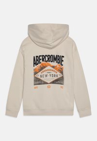 Beige hættejakke med et frontprint, der viser bjerge og tekst i sort og orange, herunder "Abercrombie, 1892, New York." Blød tekstur.