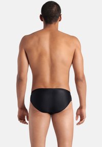 Braguitas de baño negras con una textura suave y diseño ajustado, vistas desde atrás, destacando la cintura y las aberturas para las piernas.