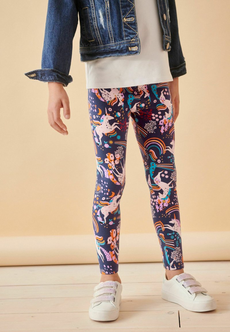 Leggings colorés avec une base marine, ornés de licornes, de fleurs et d'arcs-en-ciel. Tissu doux avec un design ajusté, associés à des baskets blanches.