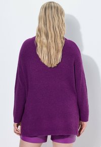 Übergroßer lila Strickpullover mit gerippter Textur, langen Ärmeln und abgerundetem Saum, kombiniert mit passenden lila Shorts.
