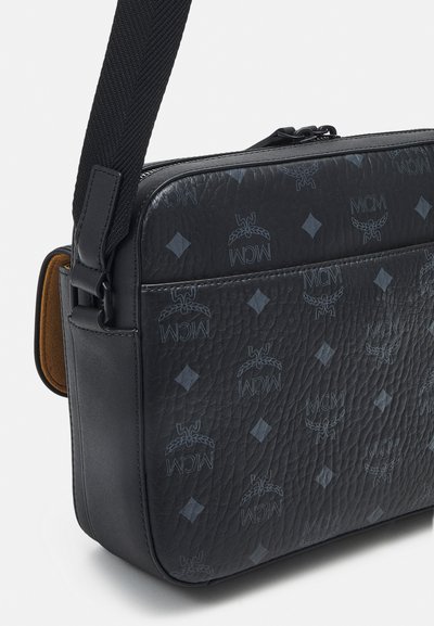 Zwarte leren schoudertas met reliëf MCM-logo en diamantpatroon, met een gestructureerde afwerking, verstelbare schouderriem en ritssluiting.