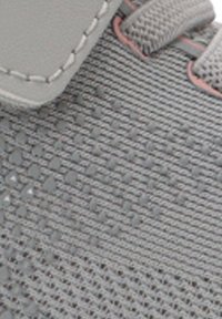 Primer plano de la parte superior de una zapatilla gris de tela con puntos de goma texturizados y detalle de cuero sintético cosido cerca de los cordones.
