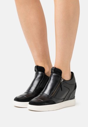 Las zapatillas de cuña de cuero negro cuentan con un zip lateral, paneles elásticos y acentos texturizados en negro. La suela es blanca, lo que proporciona un contraste con la parte superior.