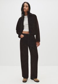 Rjava korduroj jakna in ustrezne hlače s skrajšano prileganjem. Z zip zapiranjem, žepi in mehkobo. Skupaj s svetlo rjavimi gležnjači.