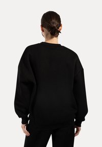 Felpa nera oversize con colletto e polsini a costine. Tessuto morbido, leggermente texture, con spalle scese per una vestibilità rilassata.