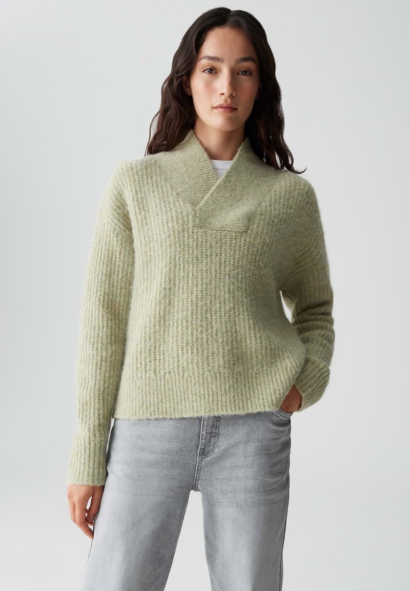 Hellgrüner Strickpullover mit einem strukturierten, gerippten Muster, einem umgeschlagenen Kragen und einer lässigen Passform, kombiniert mit hellgrauen Jeans.