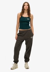 Top corto de canalé verde oscuro con detalles de encaje y botones; pantalones de chándal grises con puños elásticos y bordado "USA". Zapatillas beige.