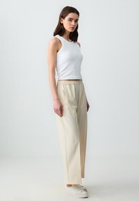 Pantaloni beige con vita elasticizzata e tasche laterali, abbinati a un top bianco aderente. Tessuto morbido con un design dritto e rilassato.