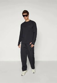 Schwarzes Langarmshirt und passende Hose aus glattem Stoff, mit einem lockeren Schnitt. Besitzt dezentes Branding, kombiniert mit hellen Sneakers.