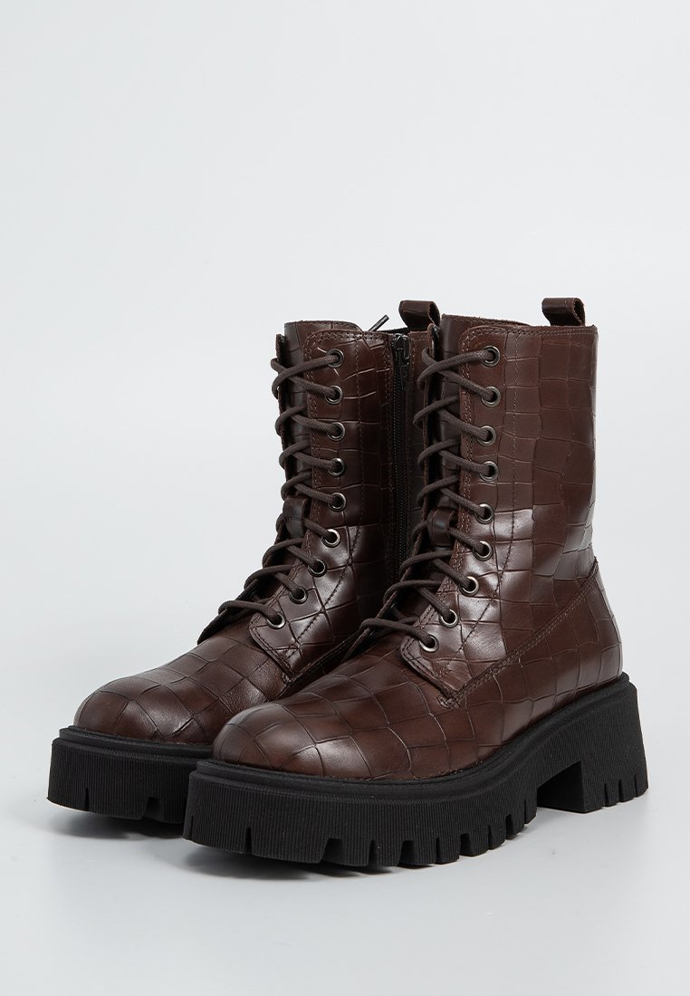 Braune Lederkampfstiefel mit Krokodilprägung, schwarzen klobigen Profilsohlen, vorderen Schnüren und seitlichen Reißverschlüssen.
