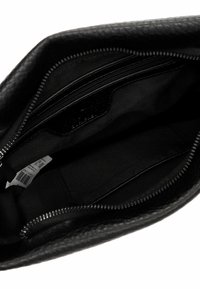 Interno di una borsa in pelle nera con tasche con zip, fodera in tessuto liscio e un'etichetta. Presenta un esterno texturizzato e una cerniera metallica.
